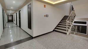 A hotel corridor with a polished floor, a staircase with metal railings, and a wall-mounted emergency exit sign. - Trulyy Rudransh inn (Jodhpur)