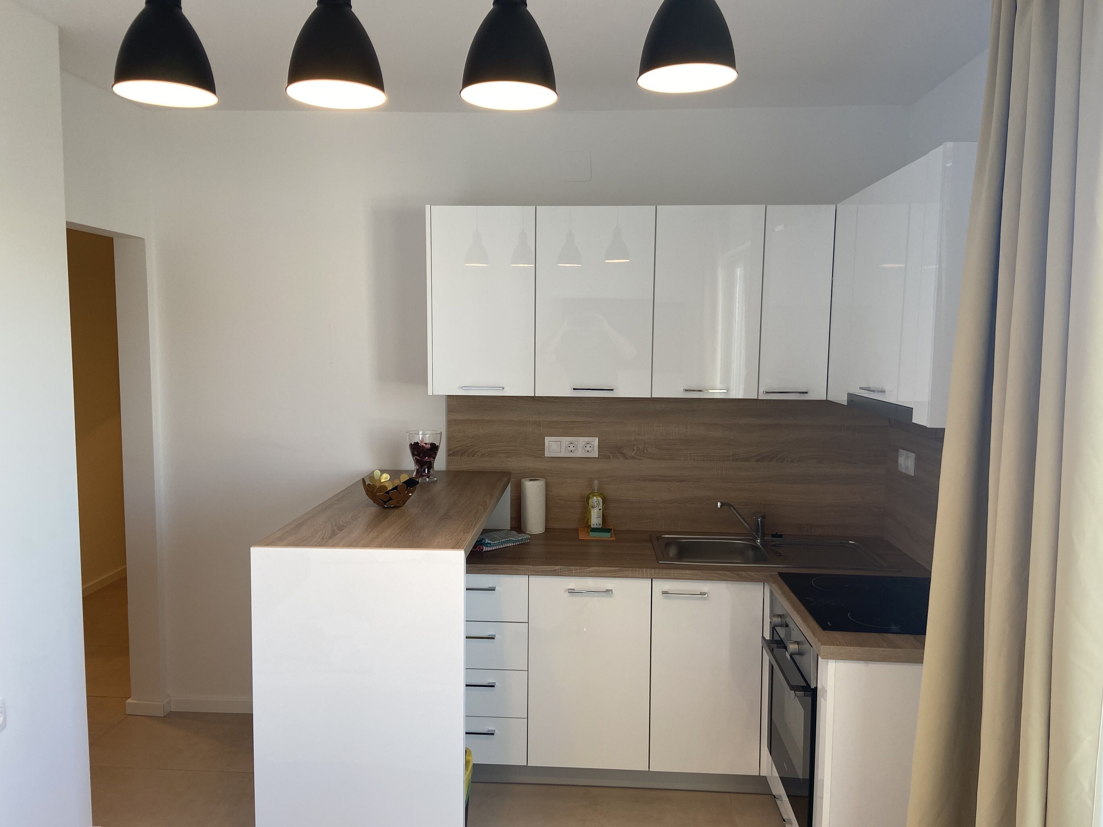Una cocina moderna con armarios blancos, encimera de madera y lámparas colgantes negras.