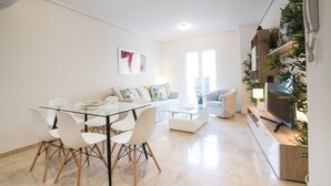 Una sala de estar moderna con una mesa de comedor de vidrio, sofás blancos y un televisor sobre un mueble de madera.
