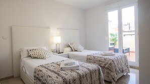 Habitación de hotel con dos camas, una mesita de noche con lámpara y una puerta corrediza de vidrio que da a un espacio al aire libre.