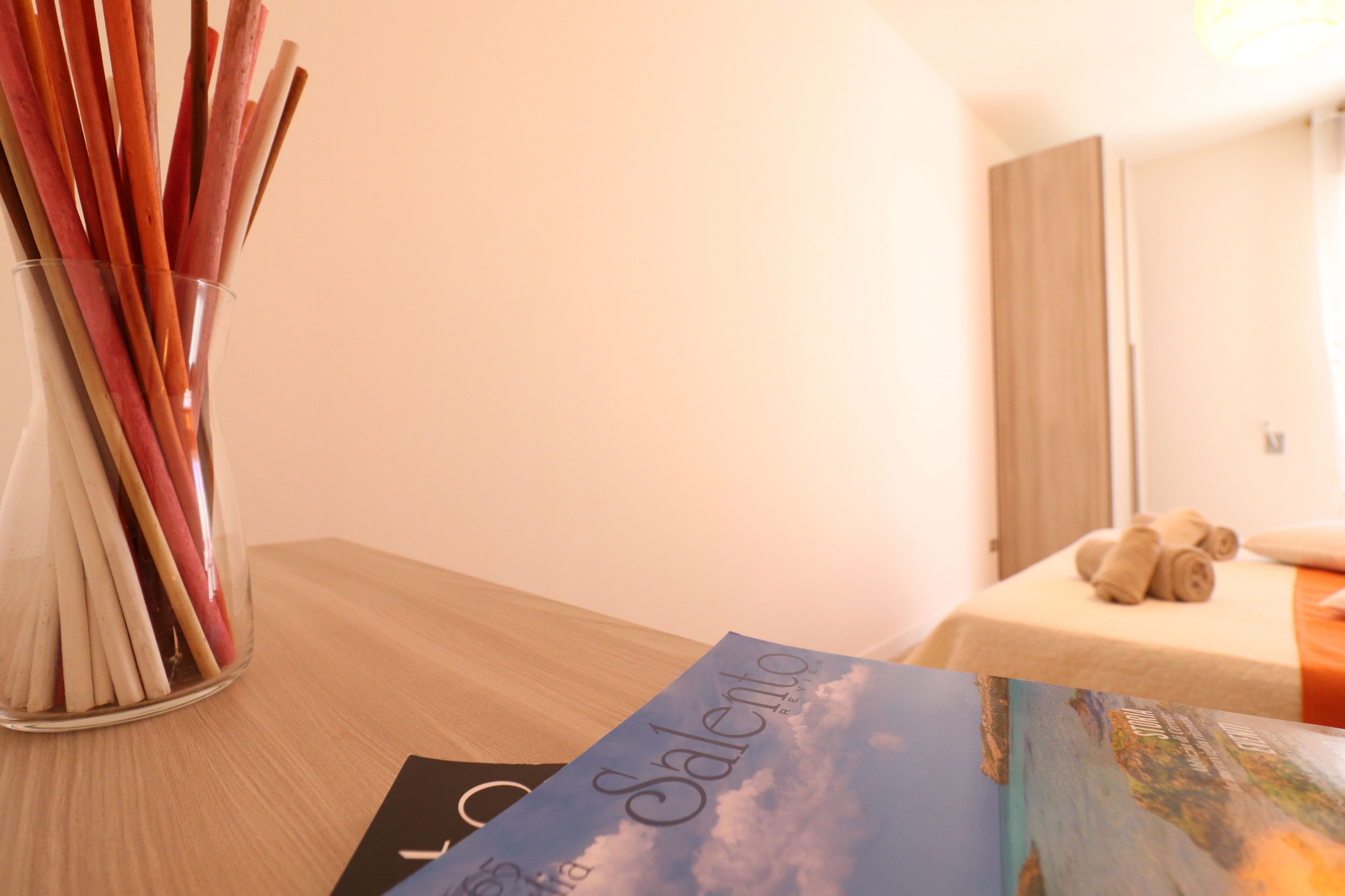 A room with a wooden table, a glass vase with sticks, and a book titled "Salento."