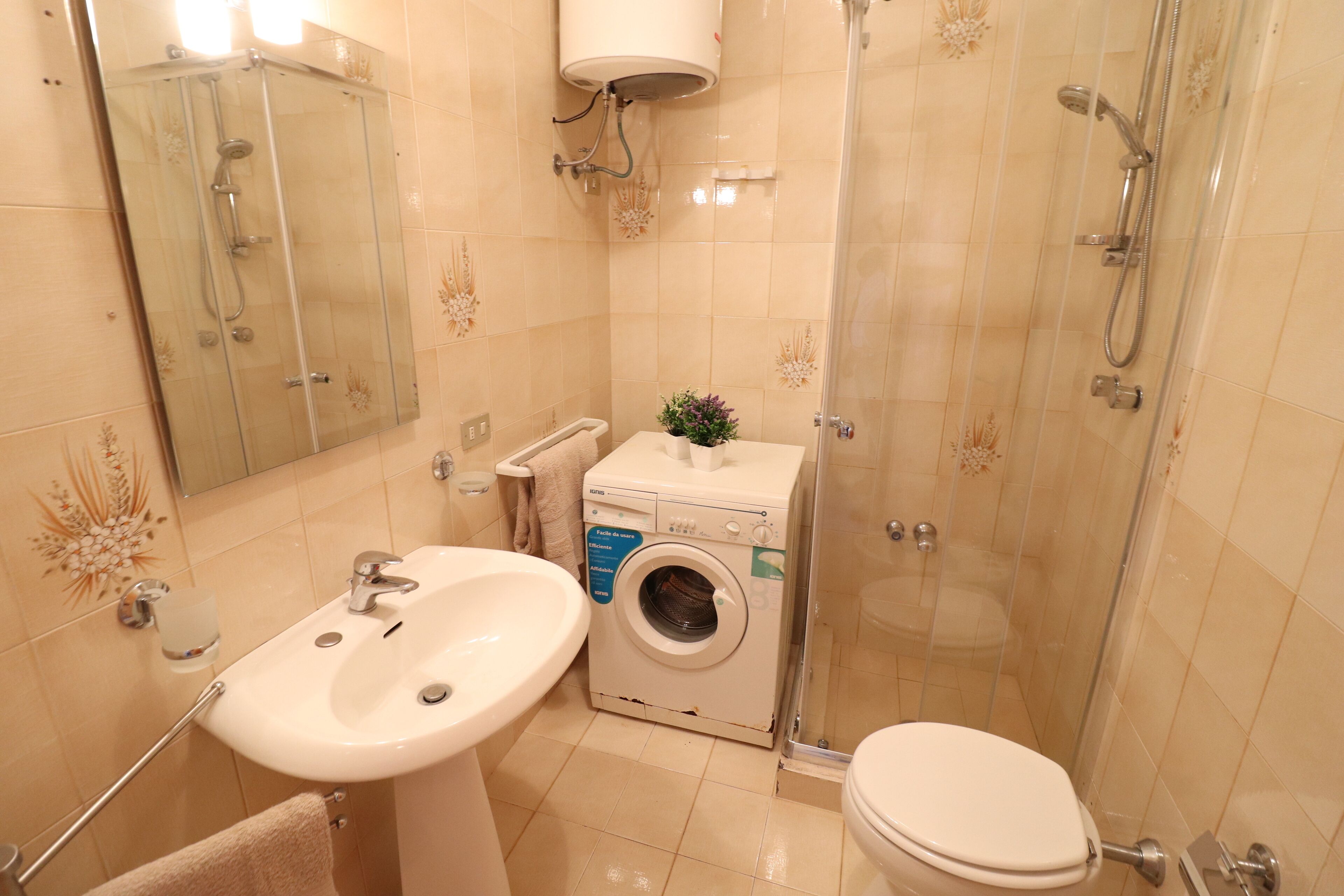 A bathroom with a sink, toilet, washing machine, and glass shower enclosure.