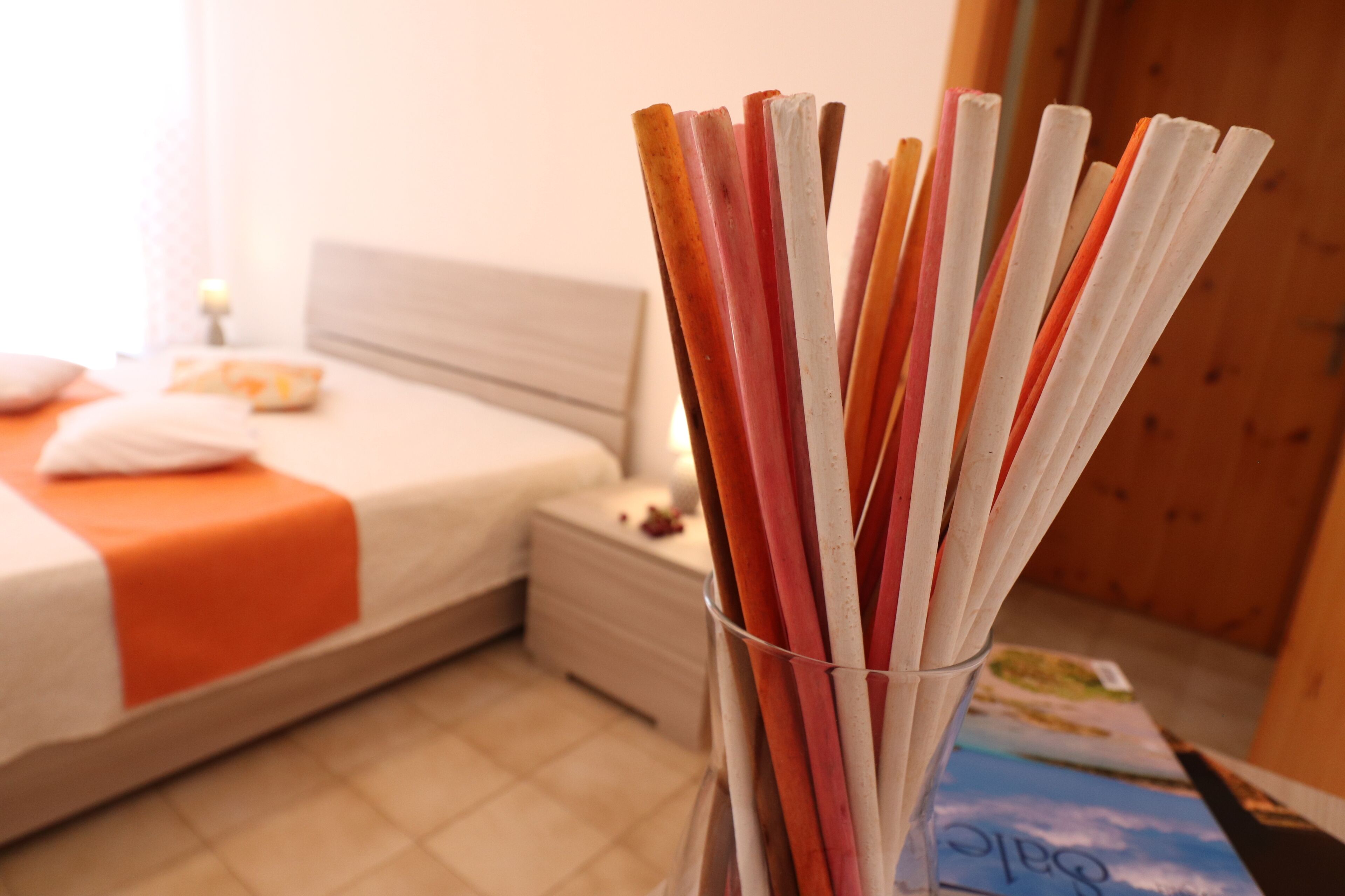 Una camera d'albergo con un letto rifatto, un comodino con una lampada e un bicchiere di paglia sul ripiano.