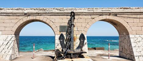 Un arco de piedra con una escultura de ancla en el centro, con vistas a la costa.