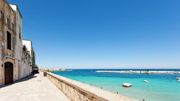 A coastal walkway with a clear view of the sea and boats, leading to a pier with a stone wall on one side and a building with a door and windows on the other. - In Good Location And With Balcony - Casa Vacanze Nicole In Salento (Otranto)