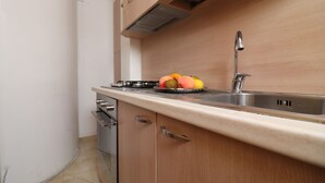 A kitchen with a stainless steel sink, wooden cabinets, and a countertop with fruits. - In Good Location And With Balcony - Casa Vacanze Nicole In Salento (Otranto)