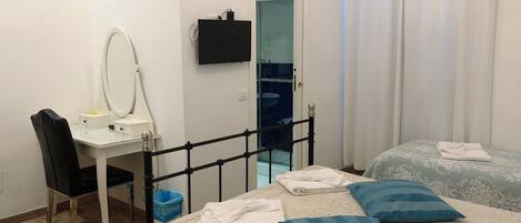 A bedroom with a bed, a desk with a mirror, a chair, and a blue trash bin.