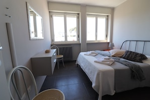 A bedroom with a bed, a desk, a chair, and two windows.