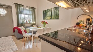 A modern kitchen with a central island, a dining area with white chairs, and a window with curtains. - Staylong Hotel (Taby)