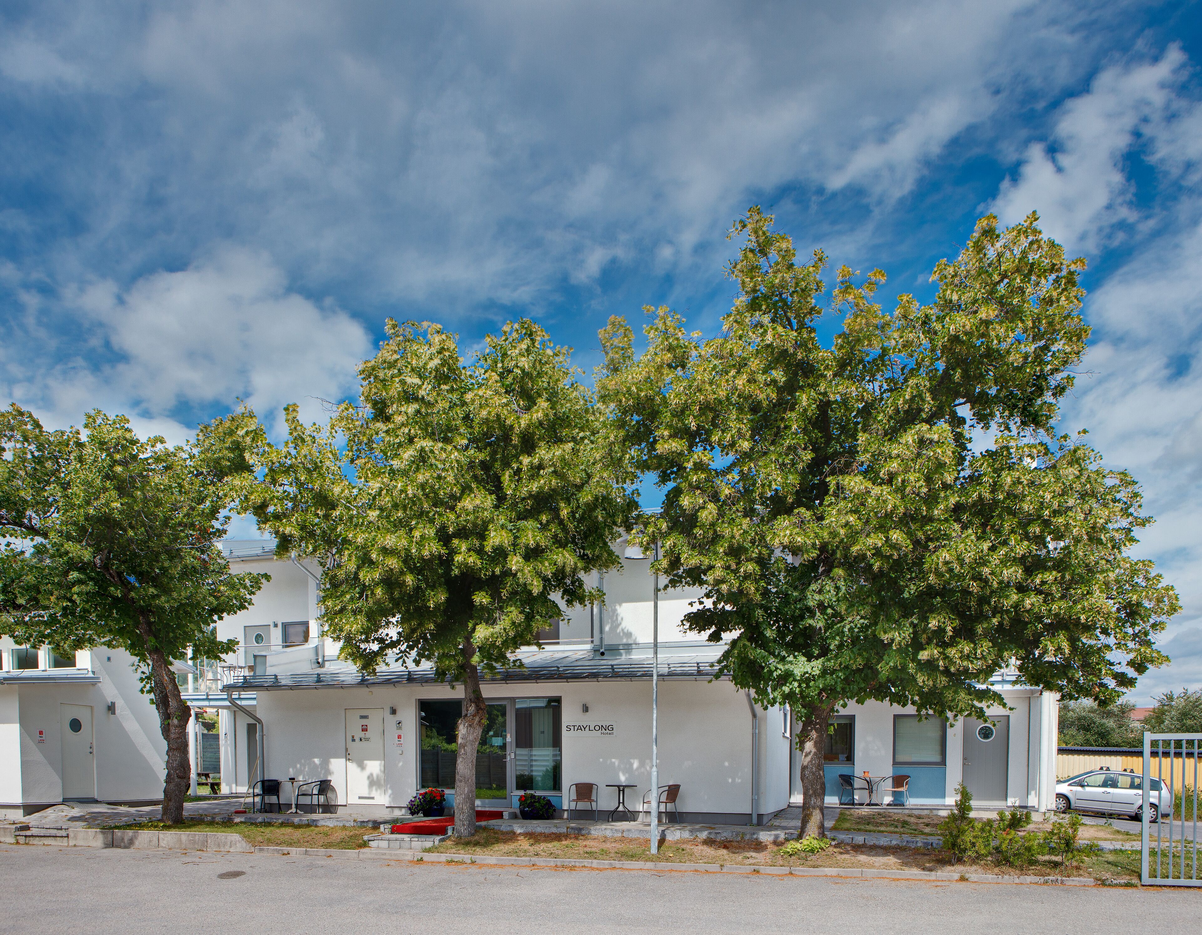 A hotel with a white exterior, a covered entrance, and a car parked outside.