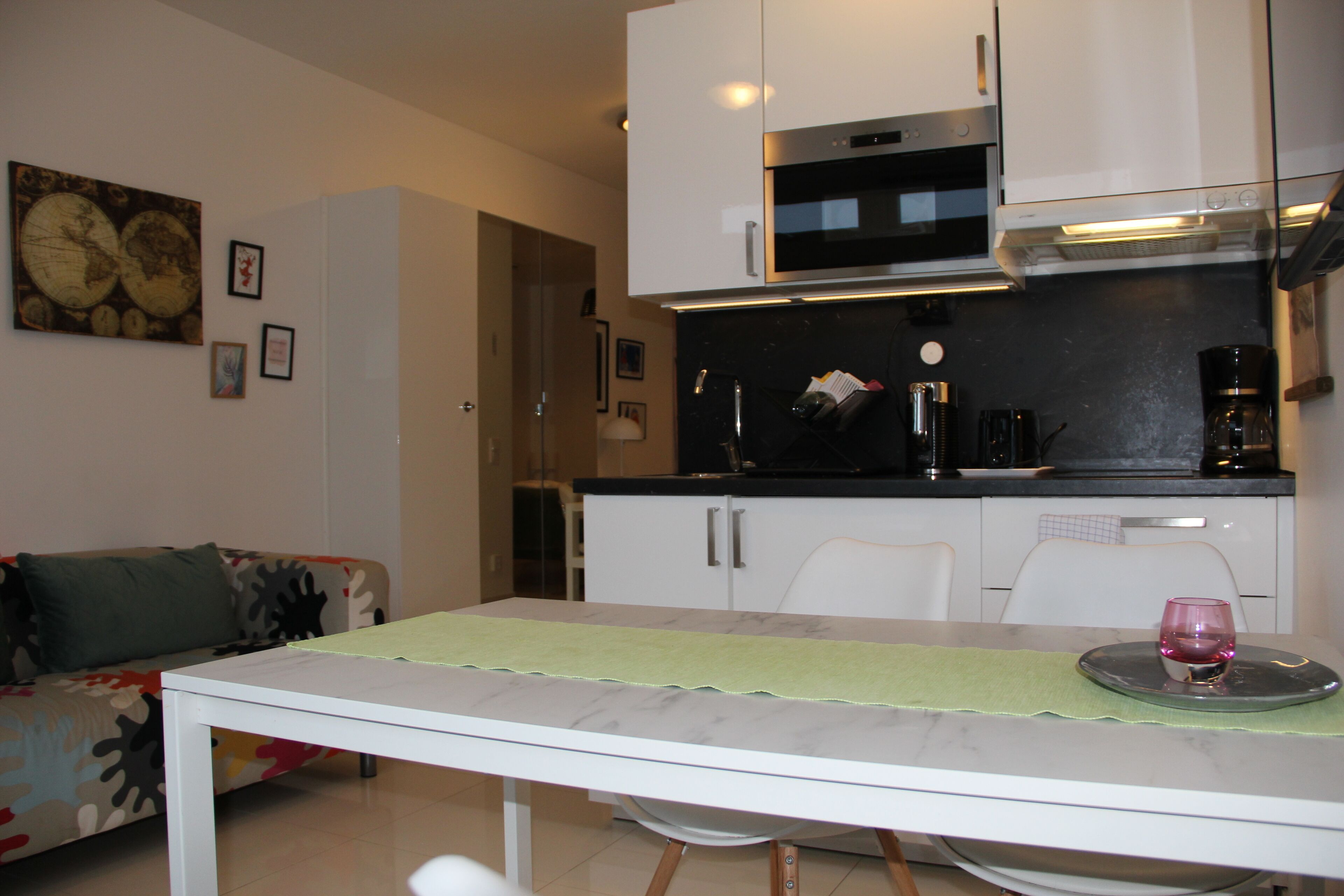 A compact kitchen with white cabinets, a black countertop, and a dining table with a green placemat.