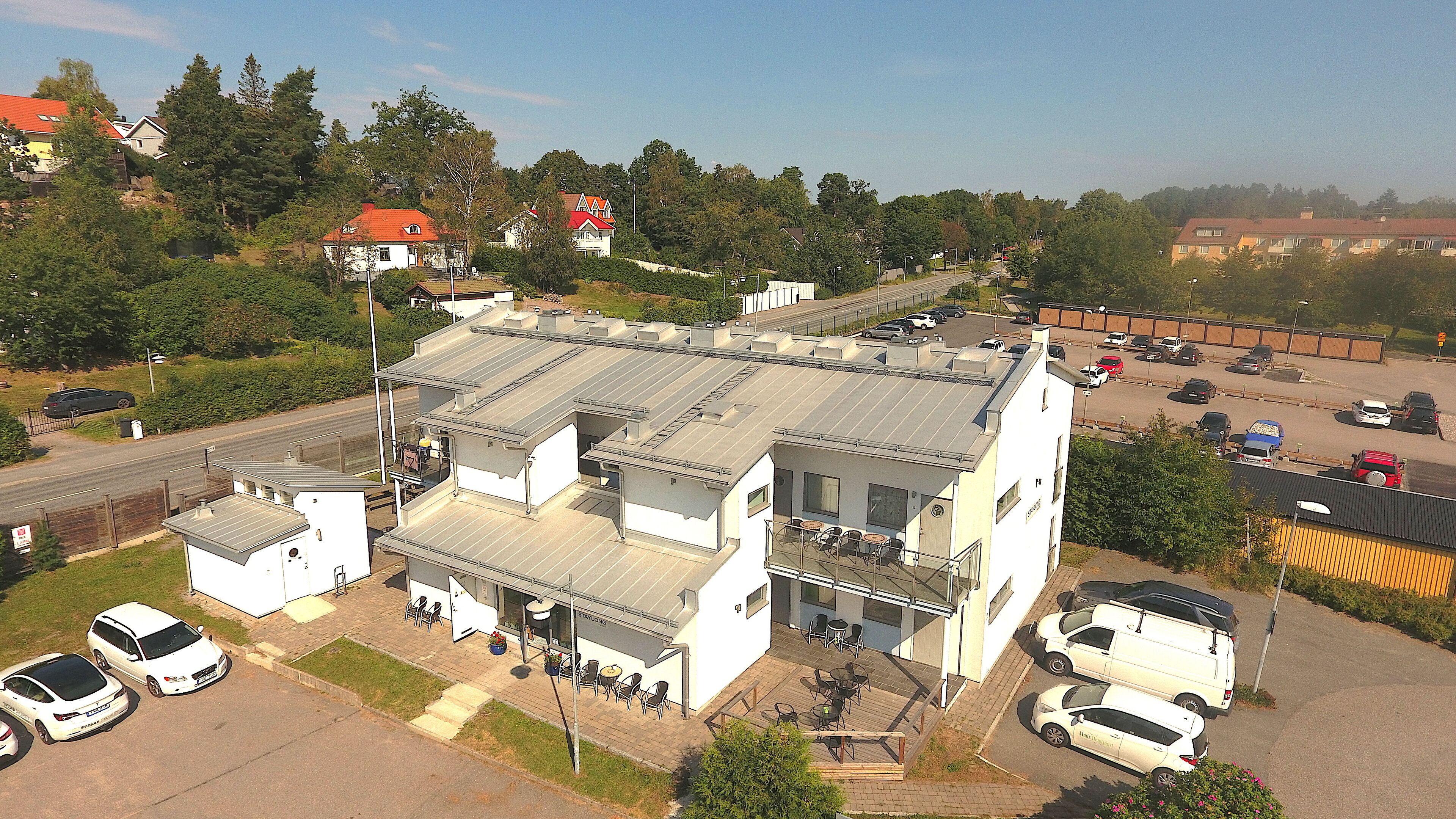 A two-story building with a flat roof and a balcony. There are several cars parked in front and around the building.