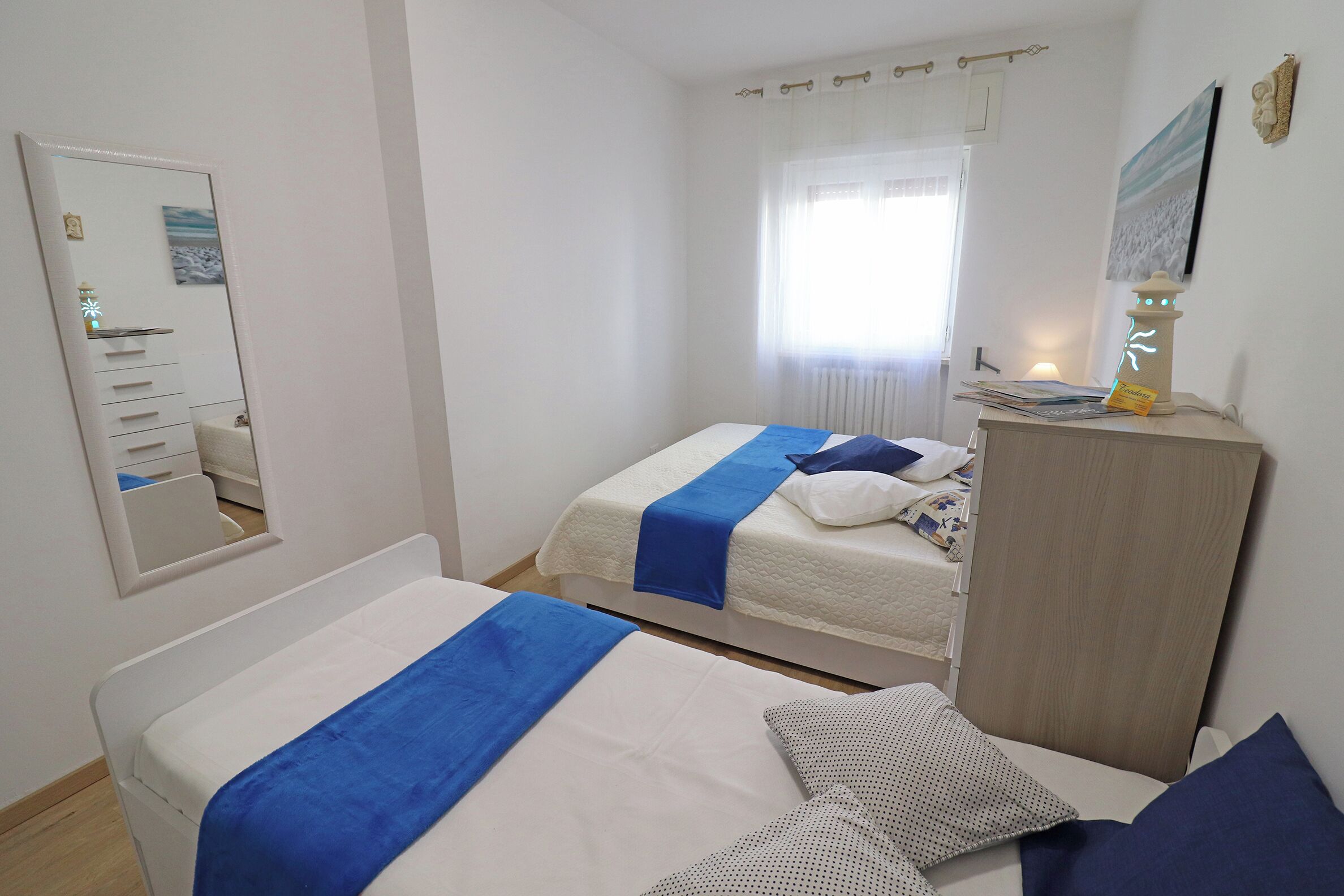 Een hotelkamer met twee bedden, een kaptafel, een spiegel en een raam met gordijnen.