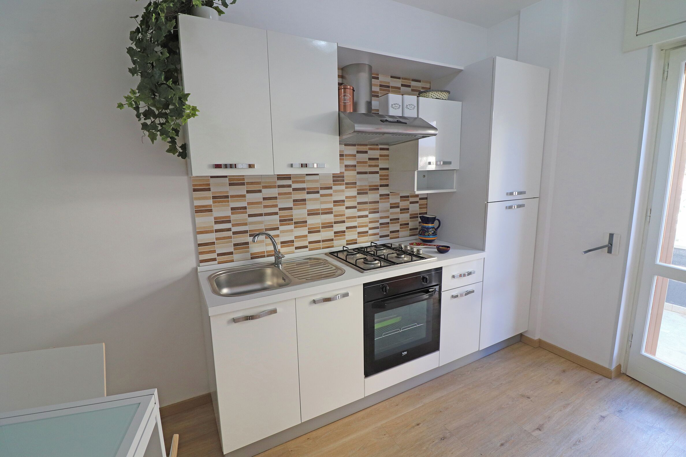 A modern kitchen with white cabinets, a gas stove, a sink, and a tiled backsplash.