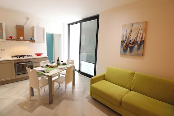 A modern kitchen with a dining area, a green sofa, and a painting of sailboats.