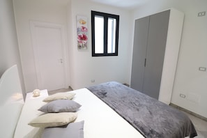 A bedroom with a bed, pillows, a wardrobe, a window, and a wall-mounted artwork.