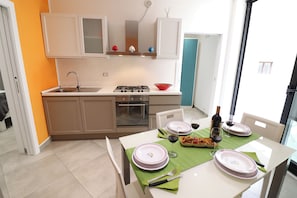A modern kitchen with a gas stove, oven, and sink. There is a dining table set with plates, glasses, and cutlery.