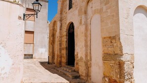 A narrow street with a building featuring a central arched doorway and a small window above it.