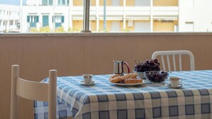 A balcony with a checkered tablecloth, a plate of pastries, a bowl of grapes, and a coffee pot.