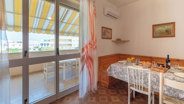 A room with a bed, a dining table, and a view through large windows.