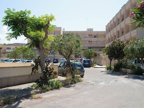 Un parking rempli de voitures, un immeuble avec des balcons et des arbres.