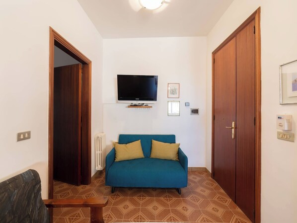 A room with a blue sofa, a television mounted on the wall, and a wooden wardrobe.