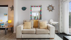 Uma sala de estar moderna com um sofá bege, um vitral colorido e decoração de parede com tema náutico.