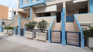 Un edificio residencial de varios pisos con fachada de tejas, entrada protegida por una reja y una escalera que conduce a la entrada.