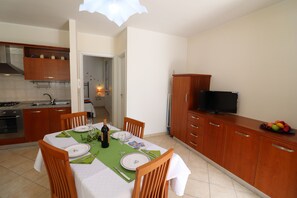 A dining area with a table set for two, a television, and a fruit bowl on the counter.