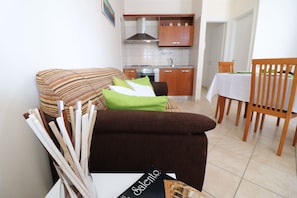 A living room with a sofa, a dining table, and a kitchen in the background.