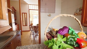 A kitchen with granite countertops, wooden cabinets, a dining area with chairs, and a basket of fresh vegetables on the counter. - Nice House Cecilia in Otranto (Otranto)
