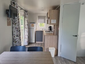 Uma cozinha compacta com geladeira, fogão e pia. Há uma mesa de jantar com cadeiras e uma janela com cortinas.