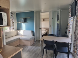 Um espaço de estar moderno e compacto, com sofá, mesa de jantar e cadeiras, pequeno espaço de cozinha e uma cama ao fundo.