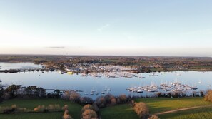 Uma marina com vários barcos atracados, cercada por campos verdes e uma cidade ao longe.