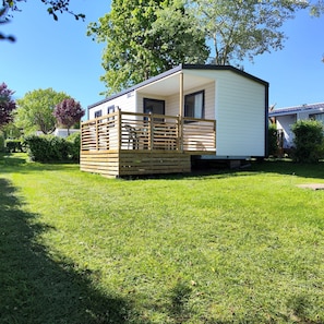 Uma casa móvel com varanda, rodeada por relva e árvores.