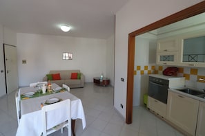 A dining area with a table set for four, a sofa, a small side table, and a kitchen with a sink and stove.