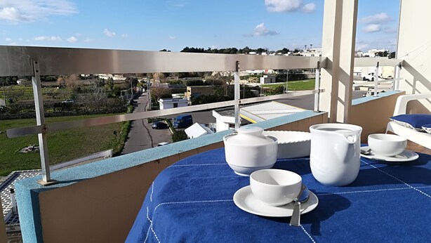 Ein Balkon mit Blick auf eine Wohngegend, ein Tisch gedeckt mit weißem Geschirr und einer blauen Tischdecke.