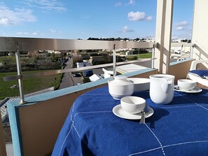 A balcony with a view of a residential area, a table set with white dishes, and a blue tablecloth.