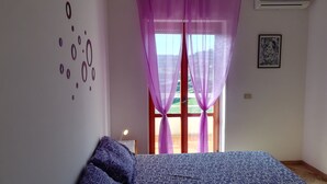 Ein Schlafzimmer mit einem Bett, violetten Vorhängen, einem Fenster mit Blick und einer Wand mit einem kreisförmigen Muster.