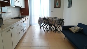 Eine kleine Küche mit weißen Schränken, einem Esstisch mit Stühlen und einem blauen Sofa.