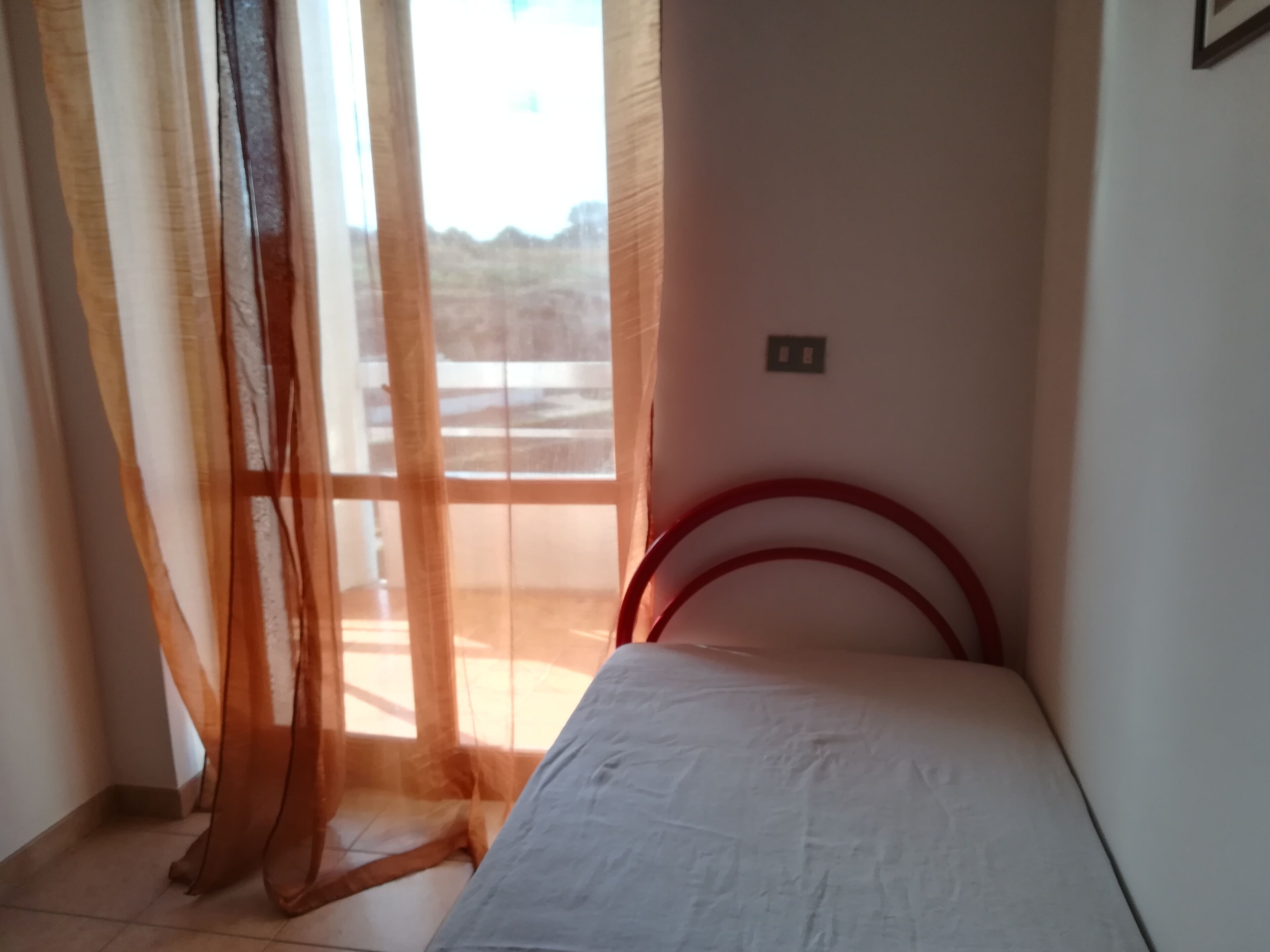 Ein Schlafzimmer mit einem Bett, transparenten Vorhängen und Blick ins Freie.