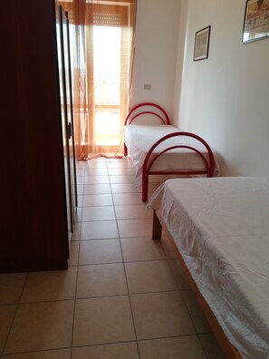 A room with two beds, a tiled floor, and a door leading to another room.