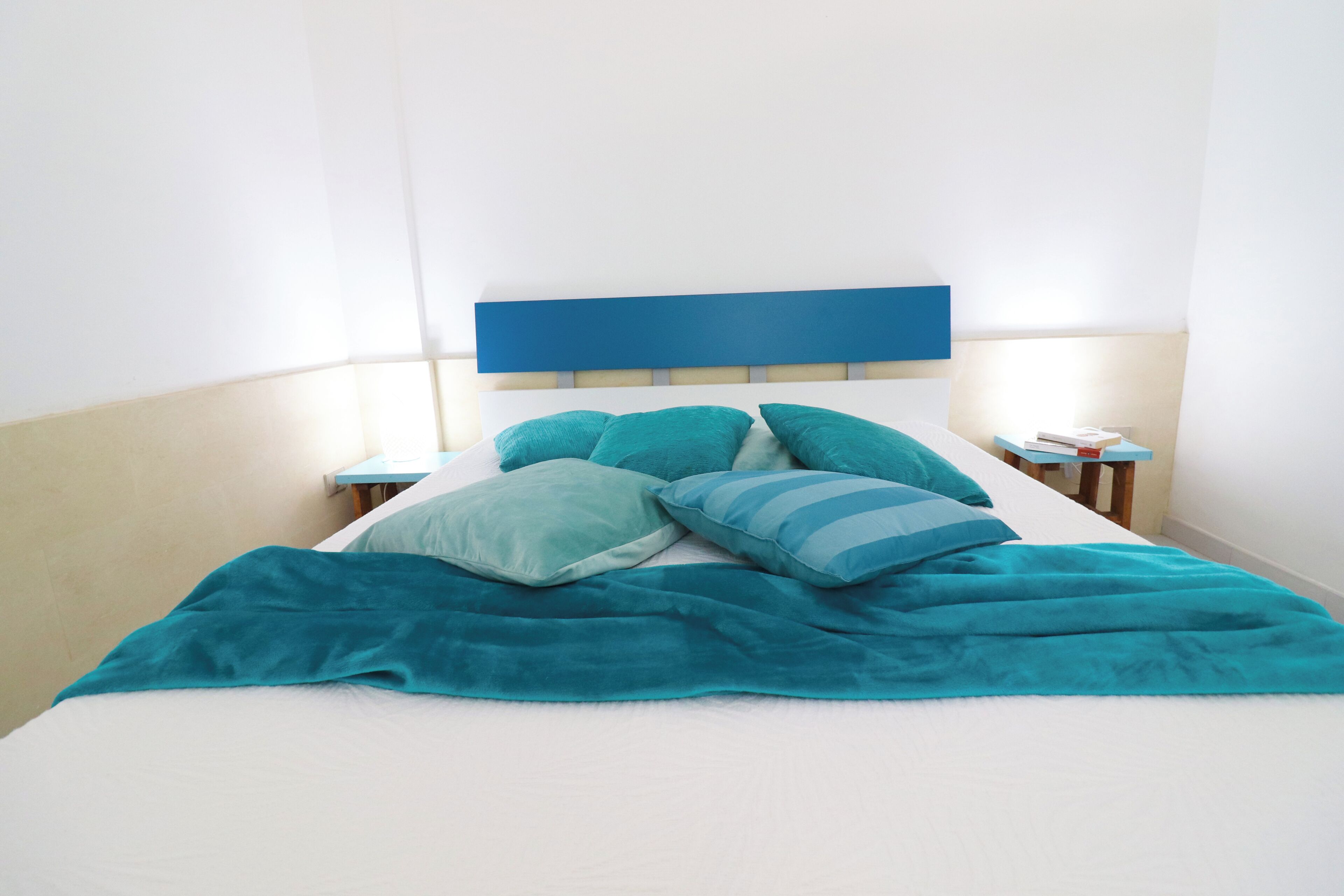 A bed with a blue headboard, teal pillows, and a teal blanket.