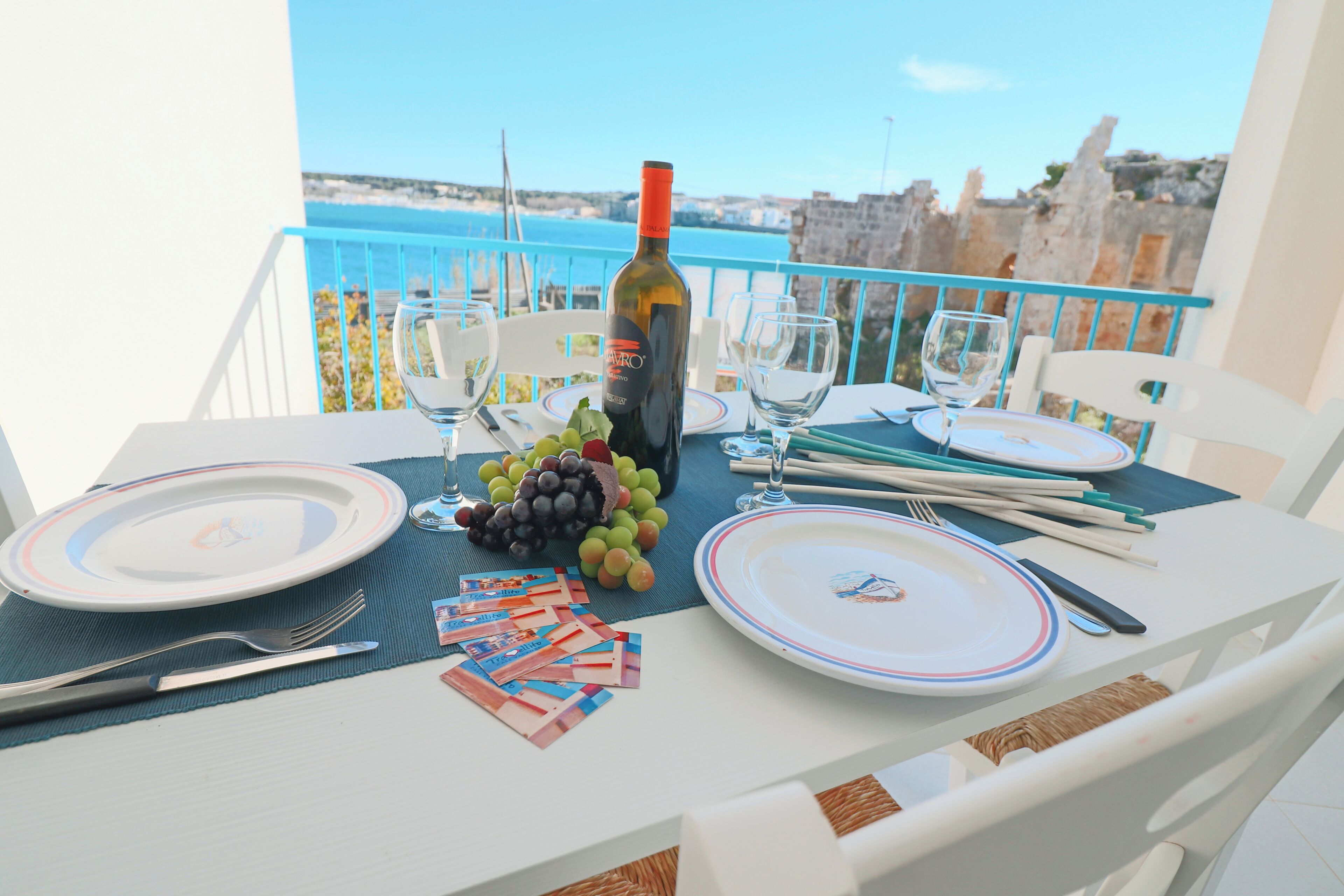 A table set for two with plates, cutlery, a bottle of wine, and a small pile of playing cards.