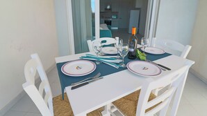 A dining table set with plates, cutlery, and a bottle, with a view of a kitchen and living area in the background. - Casa Lucrezia Unique Sea View and Relaxation Near the Historic Centre (Otranto)