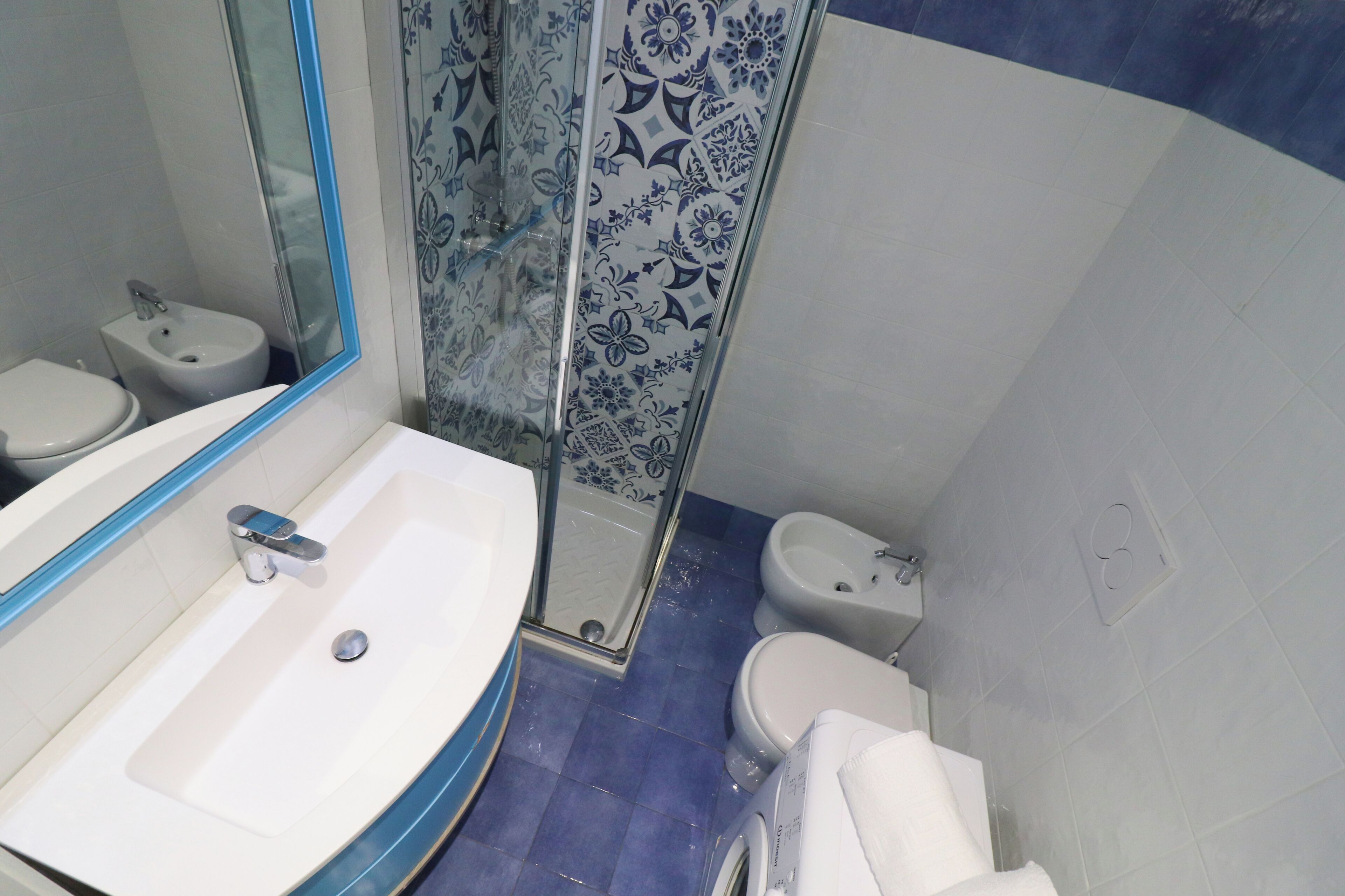 Casa de banho com lavatório branco, bidé, sanita e chuveiro com porta de vidro.