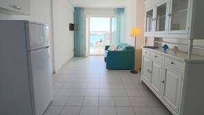 A modern kitchen with white cabinets and a refrigerator. There is a dining area with a blue sofa and a table, and a view of the sea through a large window. - Casa Lucrezia Unique Sea View and Relaxation Near the Historic Centre (Otranto)