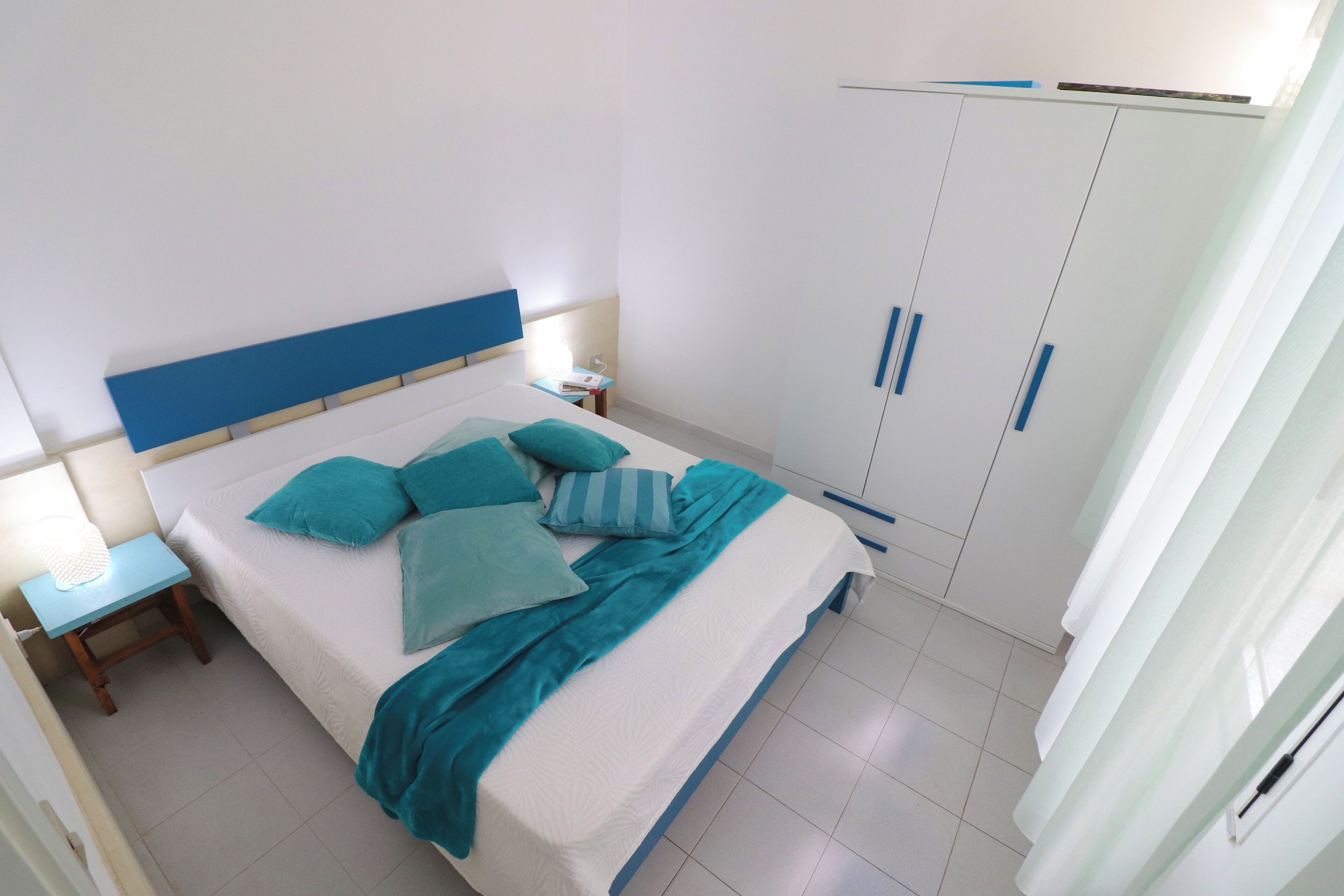 Un dormitorio con cama, mesitas de noche, armario y ventana.