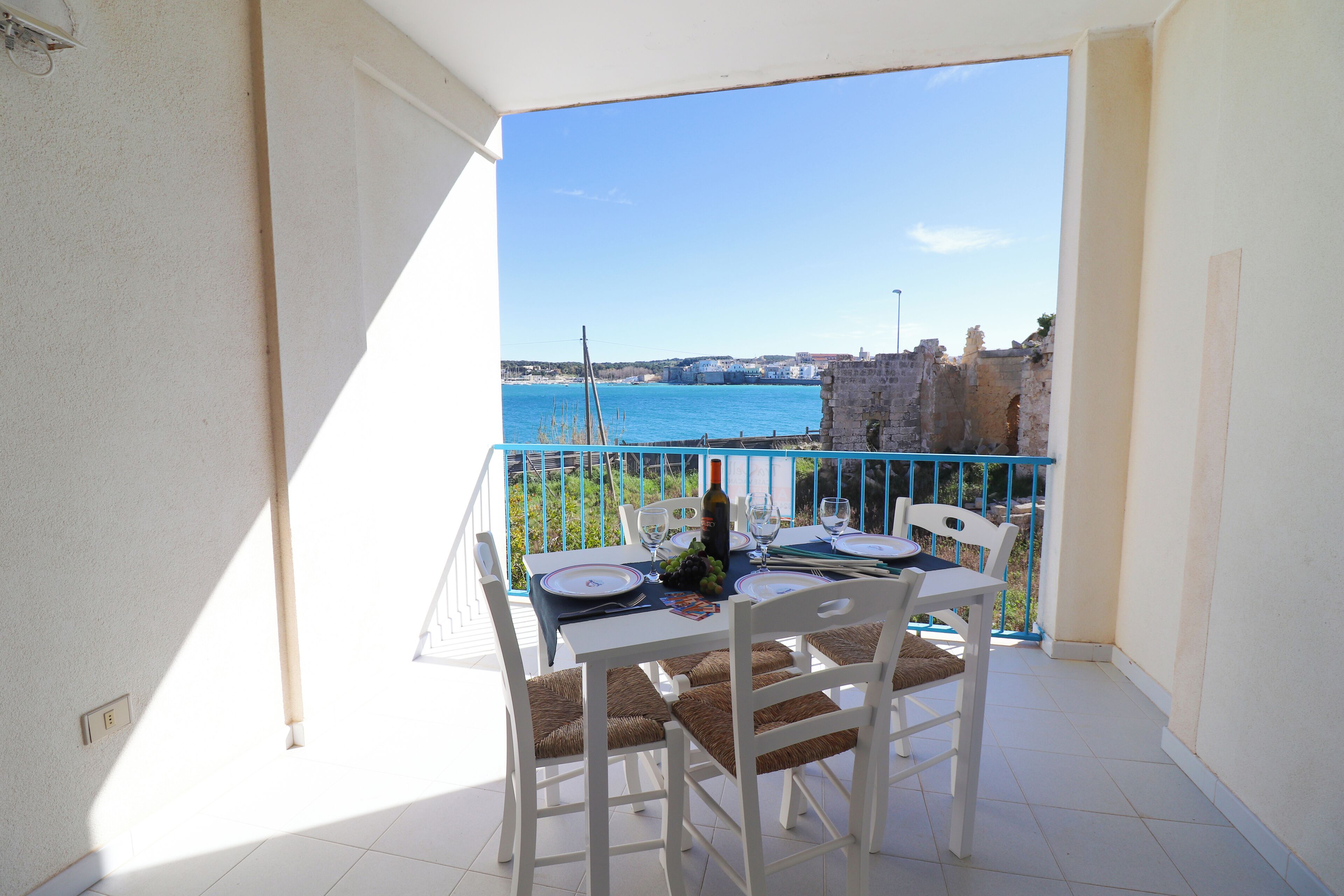 Un balcon avec une table dressée pour deux personnes, offrant une vue sur une étendue d’eau et un bâtiment historique.