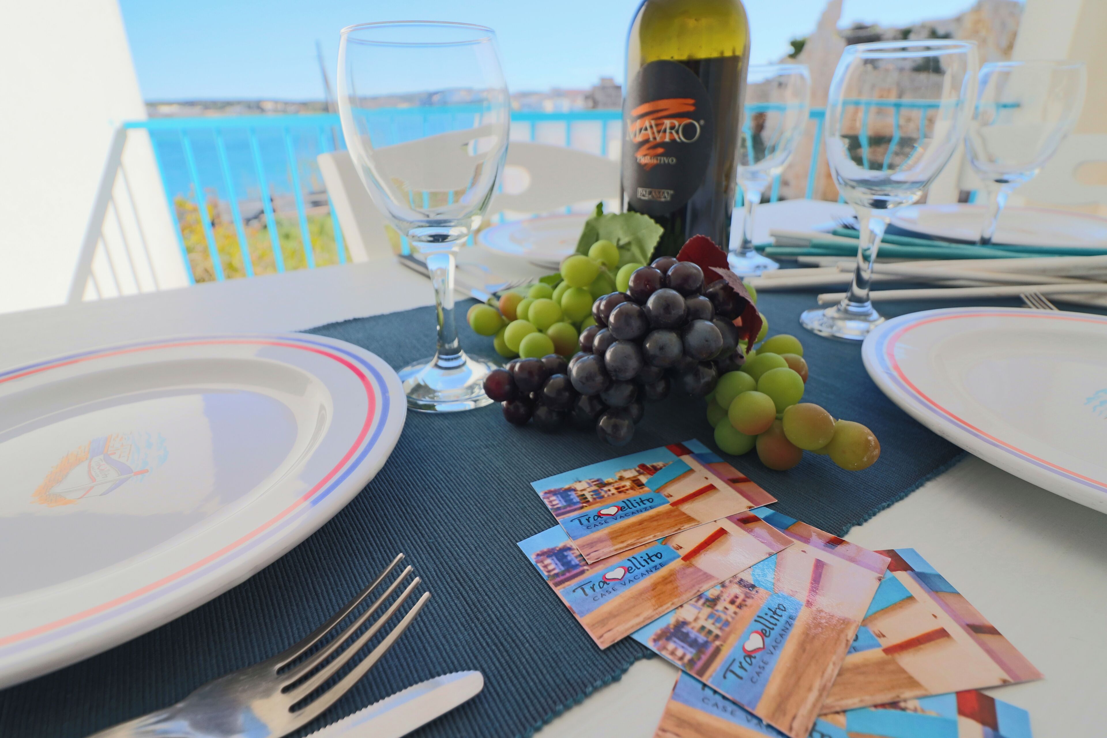 A table set for two with plates, cutlery, a bottle of wine, and a bunch of grapes.